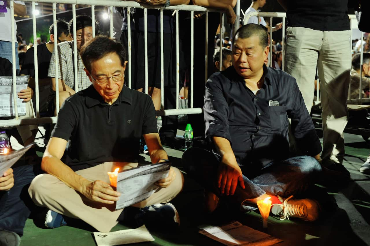 Two men sit outside. One is holding a candle.