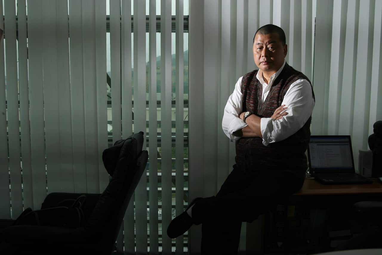 A man sits on the edge of a desk with his arms crossed.