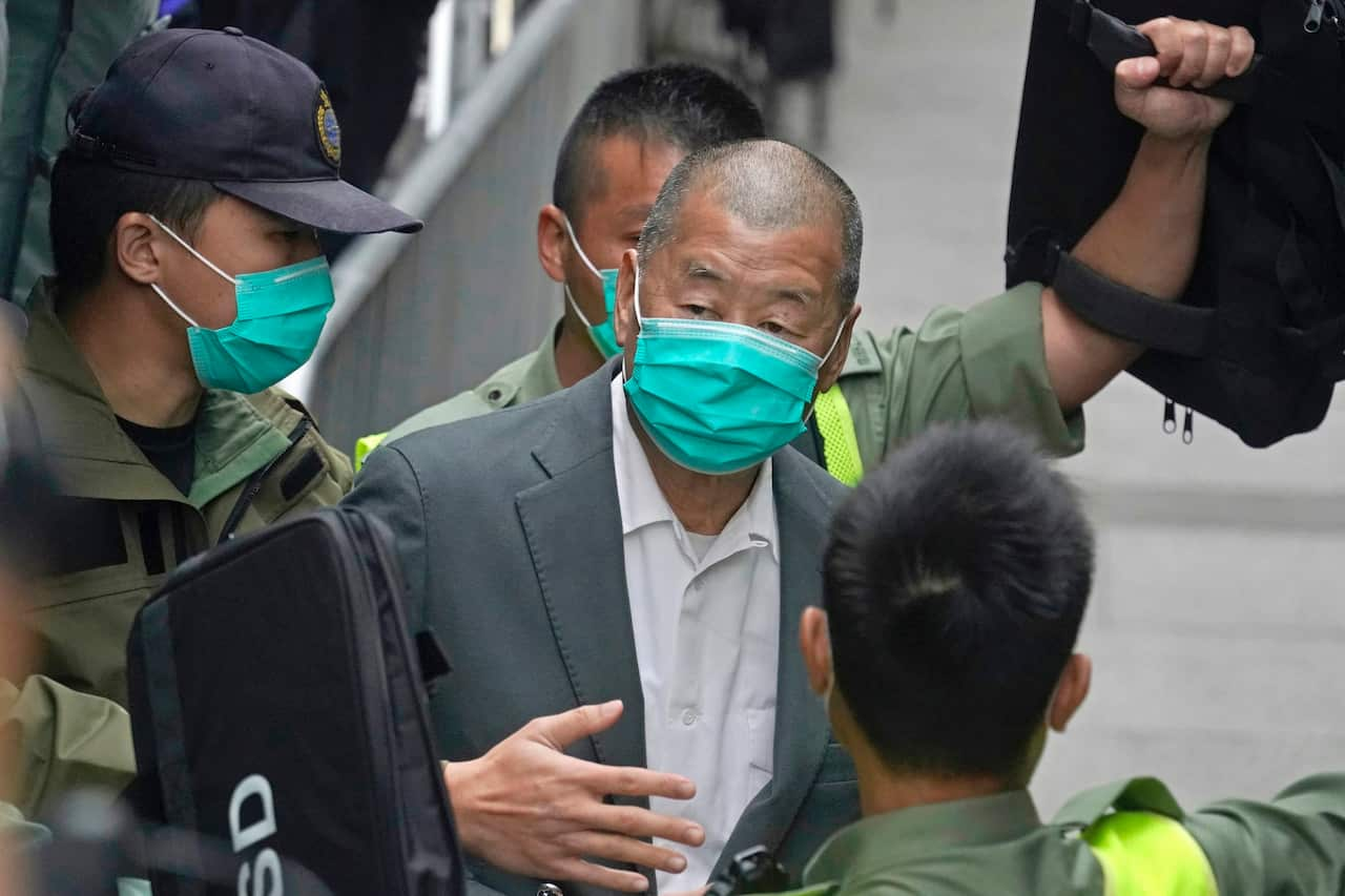 A man in a suit and wearing a green mask surrounded by three men in green uniforms  