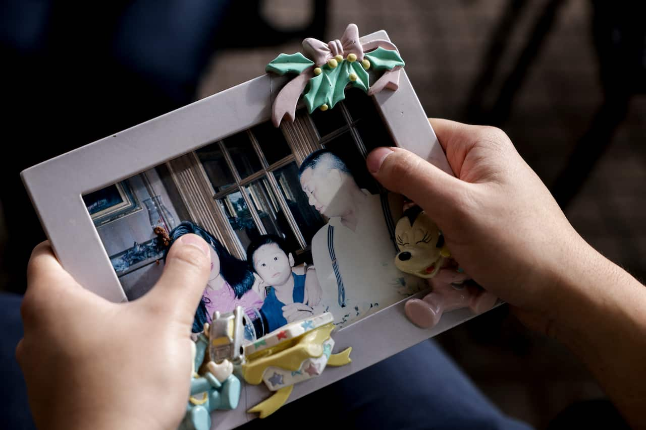 Two hands holding a photograh in a frame of a woman, a child and a man.