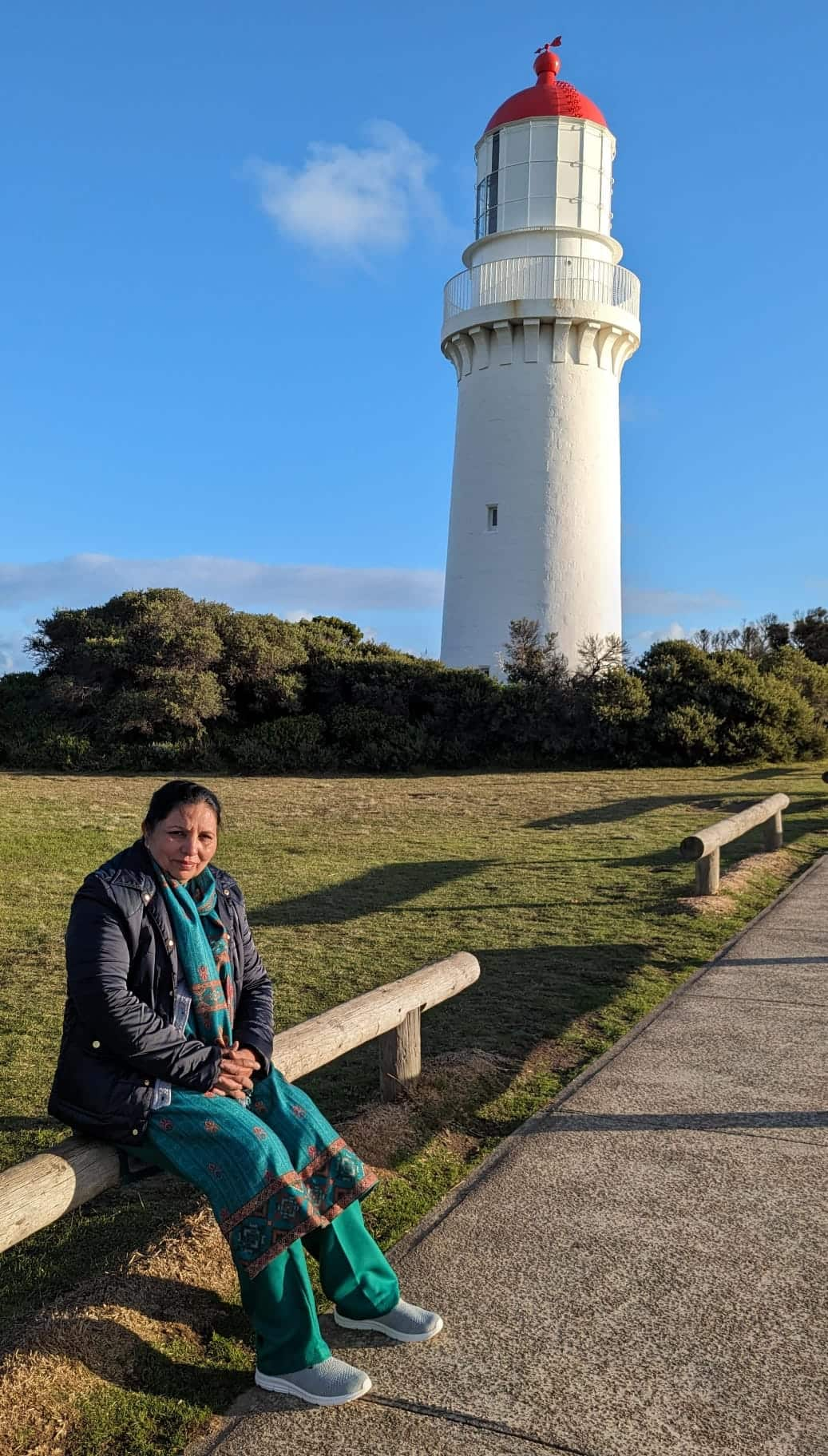 Indian migrant woman in traditional clothes sitting on the fence of a public park near a lighthouse in Victoria, Australia.