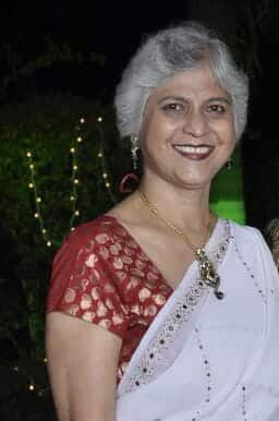 Indian woman with grey hair smiling wearing a red and white sari