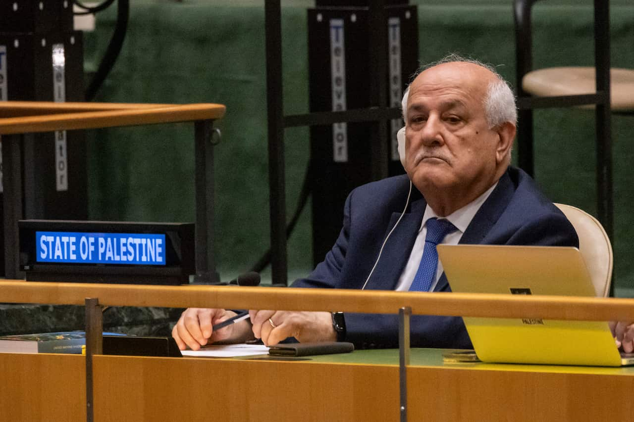 A man in a blue suit and tie sits on a bench at the UN General Assembly.