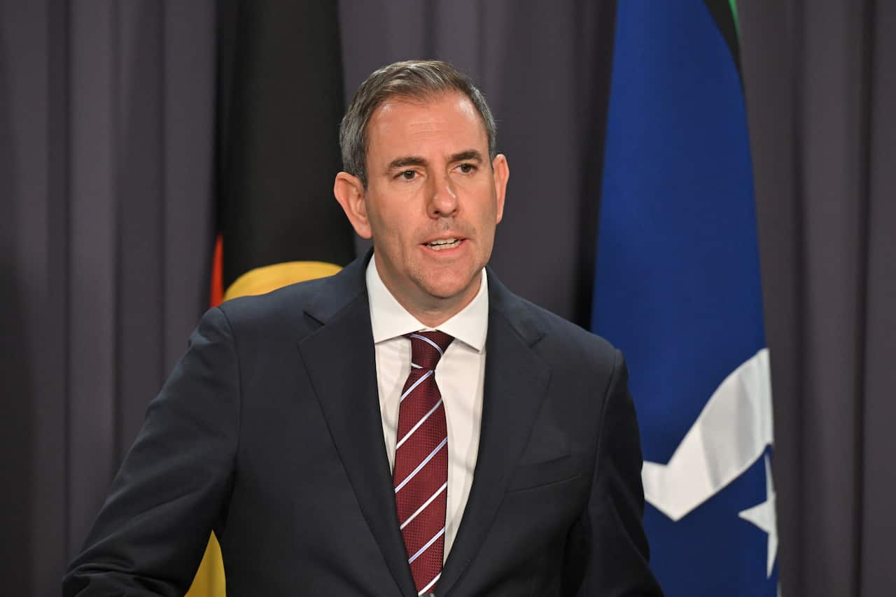 A man in a suit with a red-striped tie is speaking.