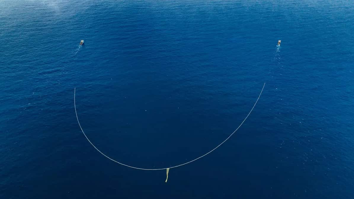 Aerial image of the ocean, with two boats travelling side by side pulling a net between them.