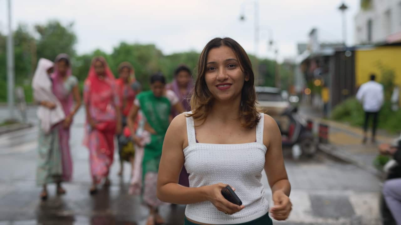 Priyanka Tamaichekar wears a low-cut white shirt and smiles to camera. 