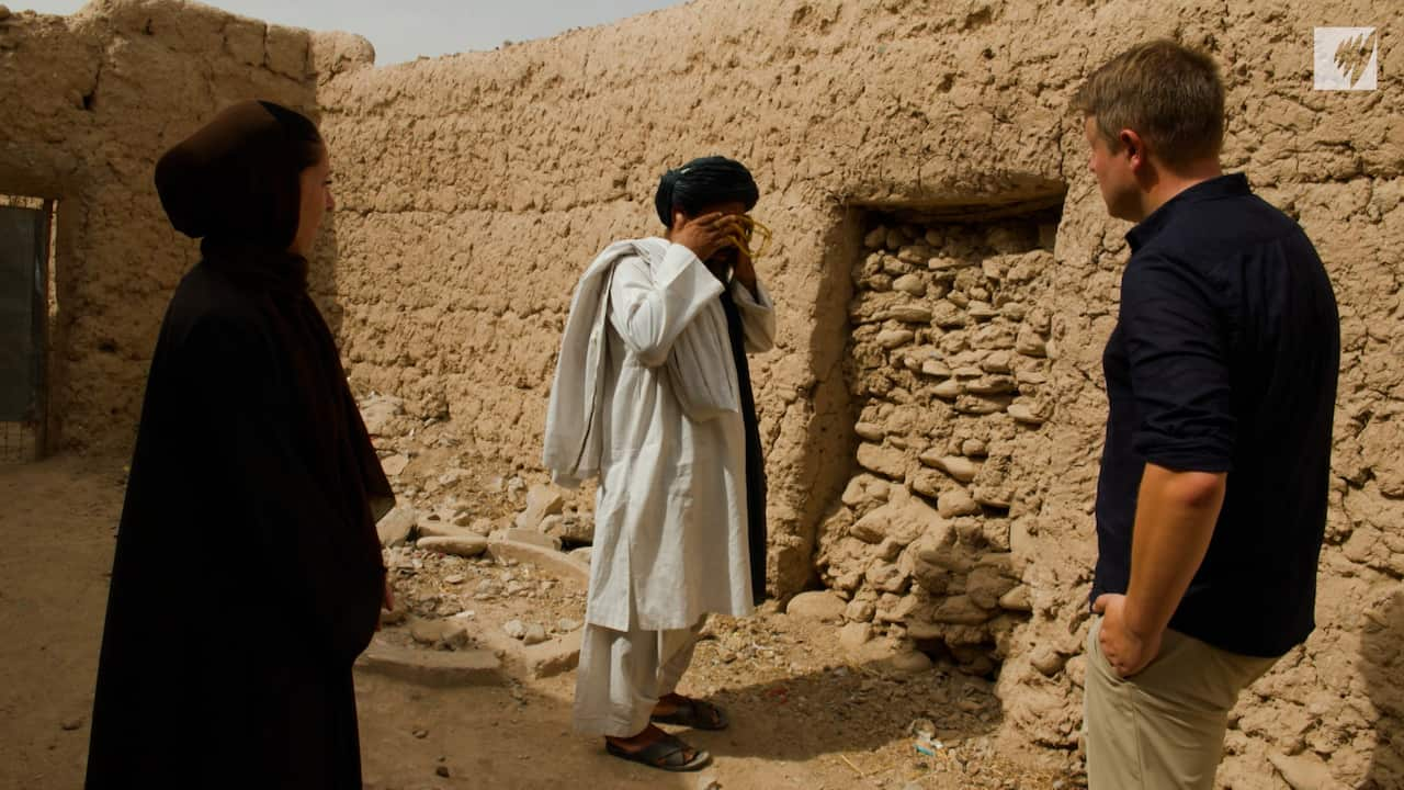 Haji Gul Mohammad in white robes covers his eyes in front of the mud walls of the couryard