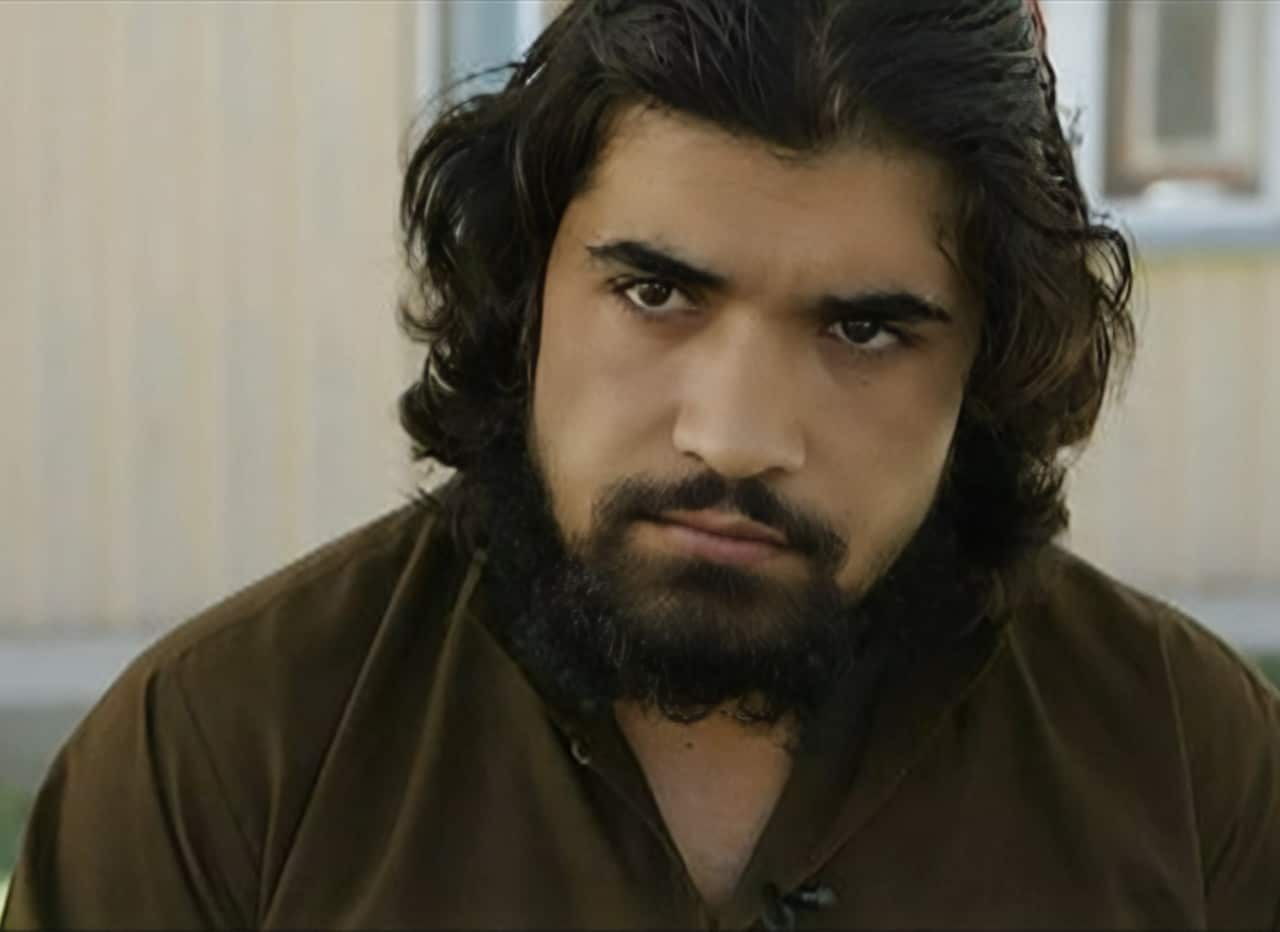 hekmatullah wears a brown shirt with shoulder length hair and a dark beard. 