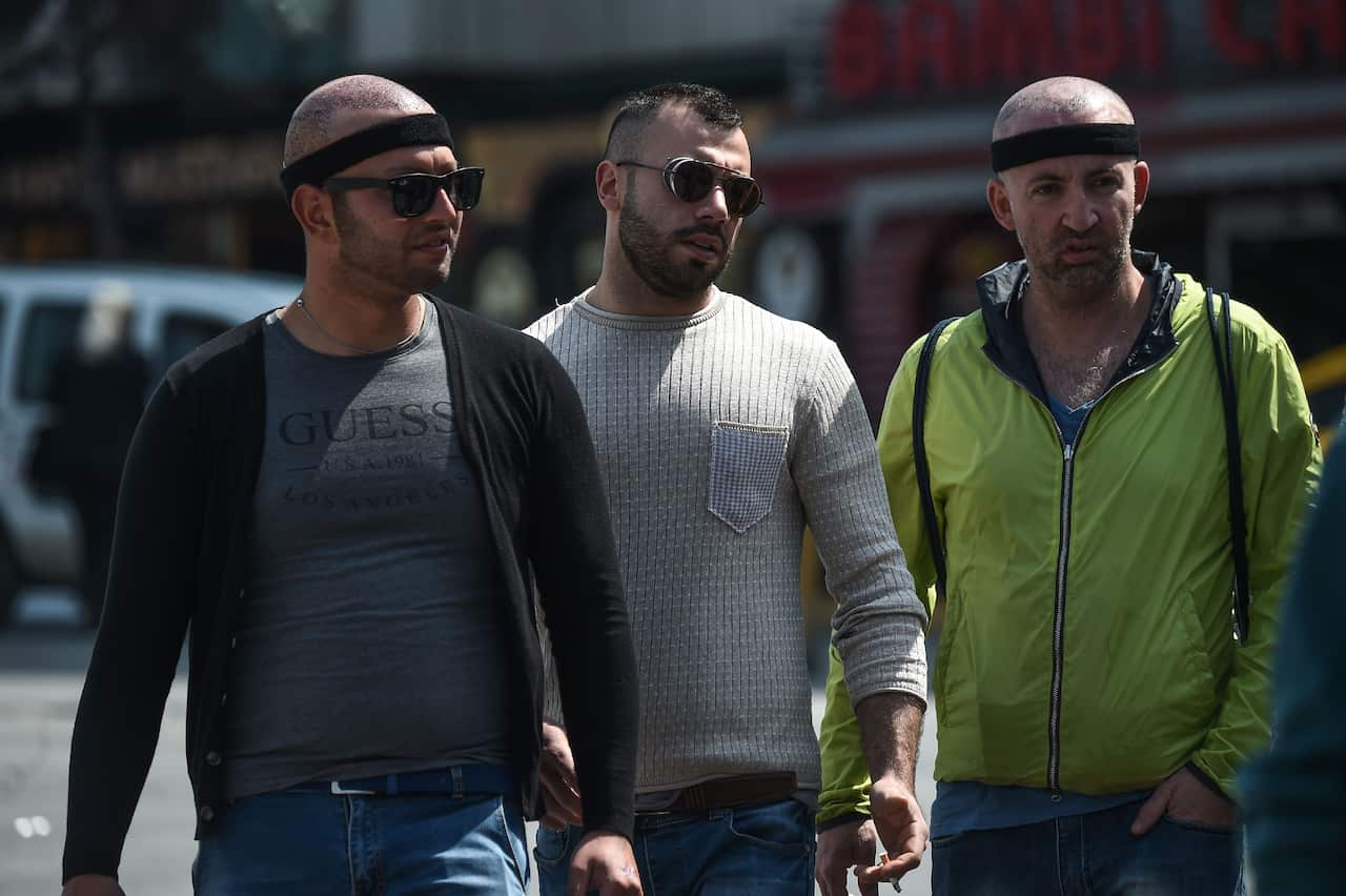 Two men wear a black headband while another man walks beside them.