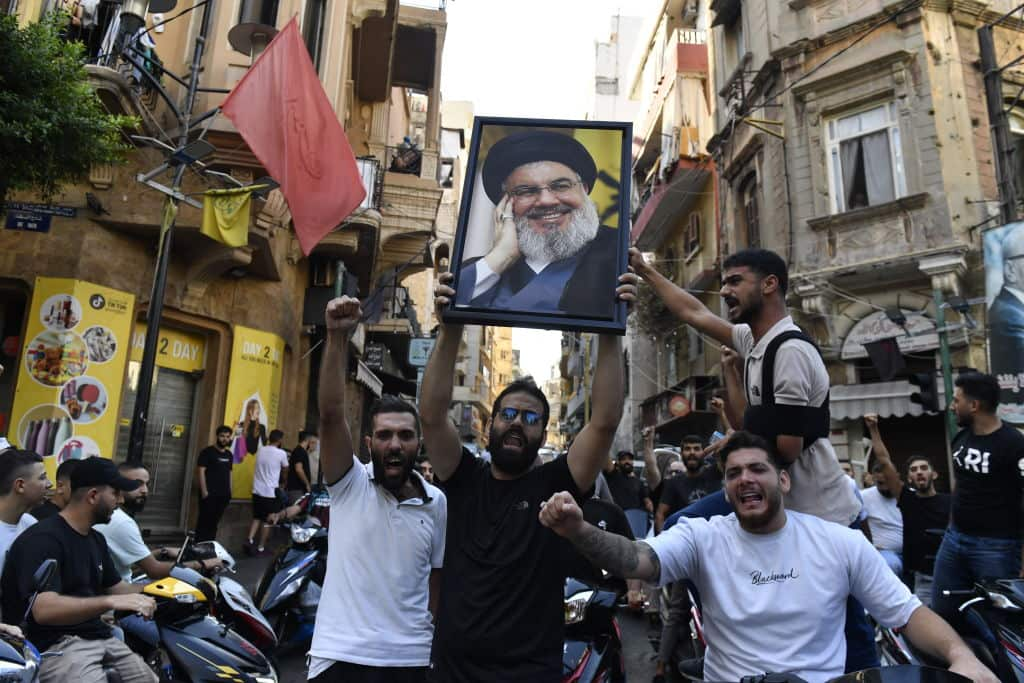 A group gather carrying former Hezbollah leader Hassan Nasrallah's poster and chanting slogans.